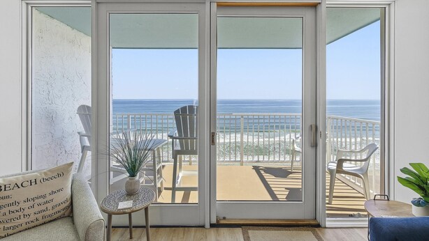 Una habitación con puerta corrediza de vidrio que da a un balcón con vistas a la playa.