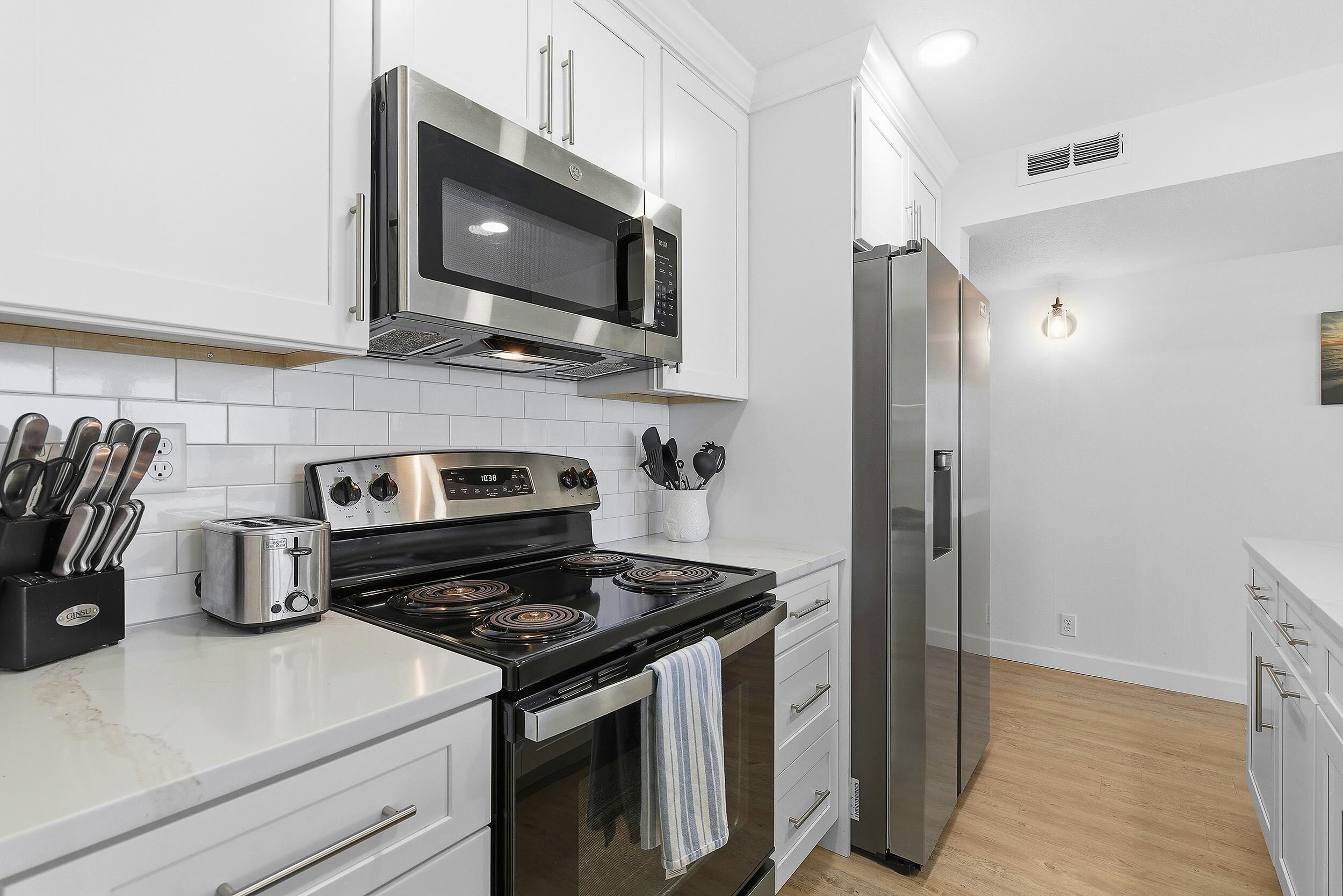 A modern kitchen with white cabinets, stainless steel appliances, and a wooden floor.