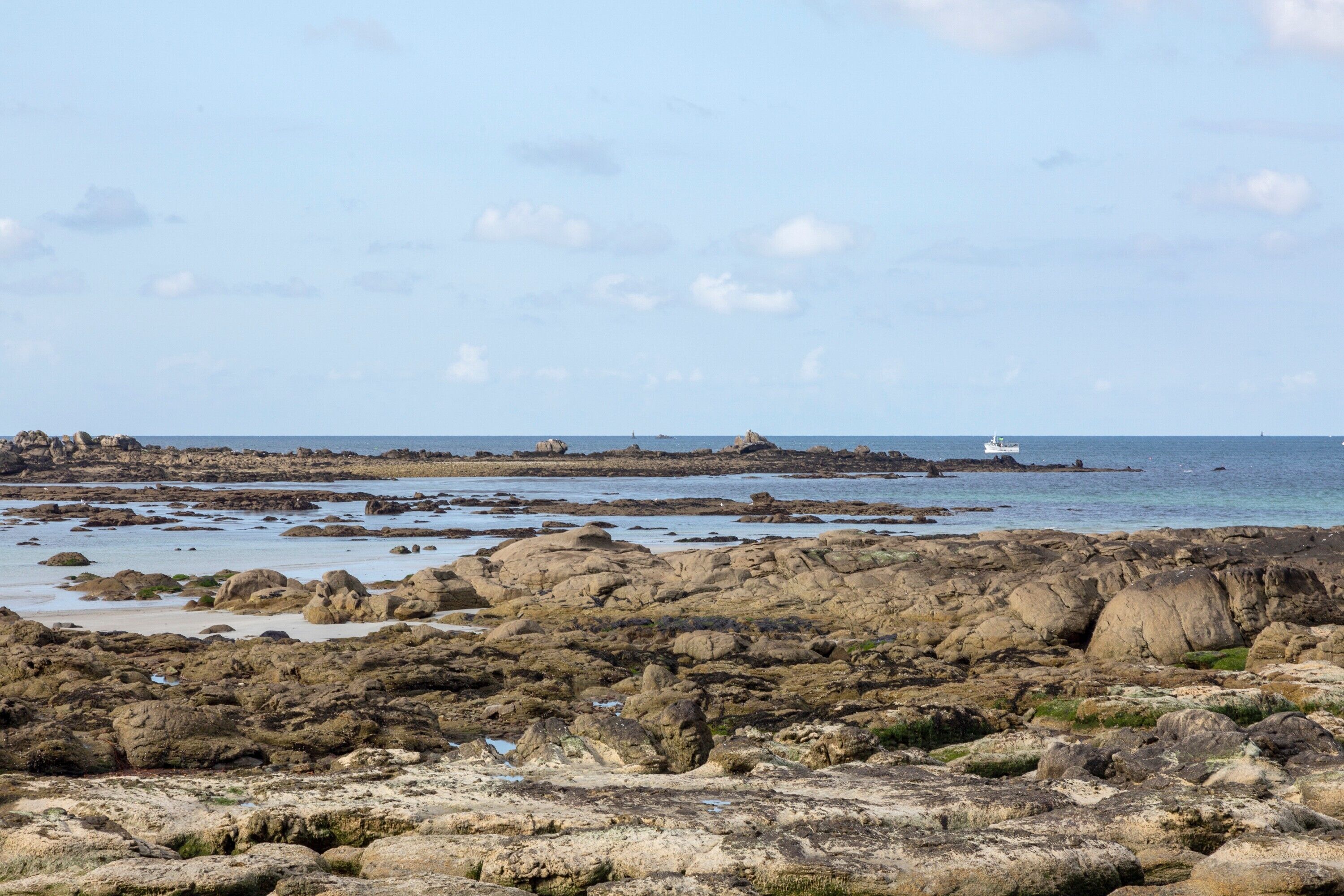 Un paysage côtier rocheux, avec un phare visible au loin.