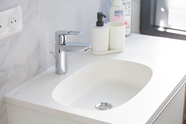 A bathroom with a white sink, chrome faucet, and a soap dispenser.