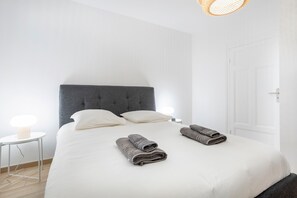 A neatly made bed with pillows, a bedside table with a lamp, and a door in a simple, clean room. - Ty Mor Holiday Home – Superb 1-Bedroom Apartment in the Heart of Guilvinec with Wi-Fi (Guilvinec)