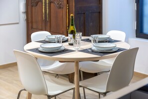 A round dining table with white chairs, a bottle of champagne, and clear glasses on a beige tablecloth. - Ty Mor Holiday Home – Superb 1-Bedroom Apartment in the Heart of Guilvinec with Wi-Fi (Guilvinec)