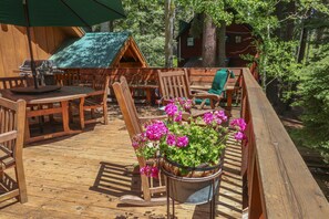 Una terraza de madera con mobiliario exterior, una parrilla y una maceta con flores.