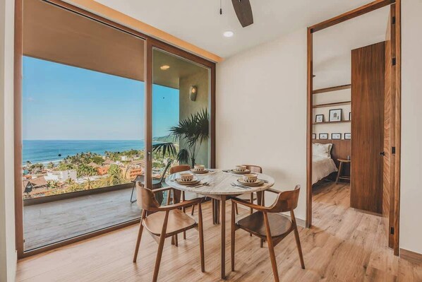Un espace repas avec vue sur l’océan, un plancher en bois et un ventilateur de plafond.