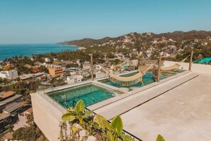 Une piscine située sur le toit, avec une eau d’un bleu limpide, entourée de bâtiments et offrant une vue sur la côte.