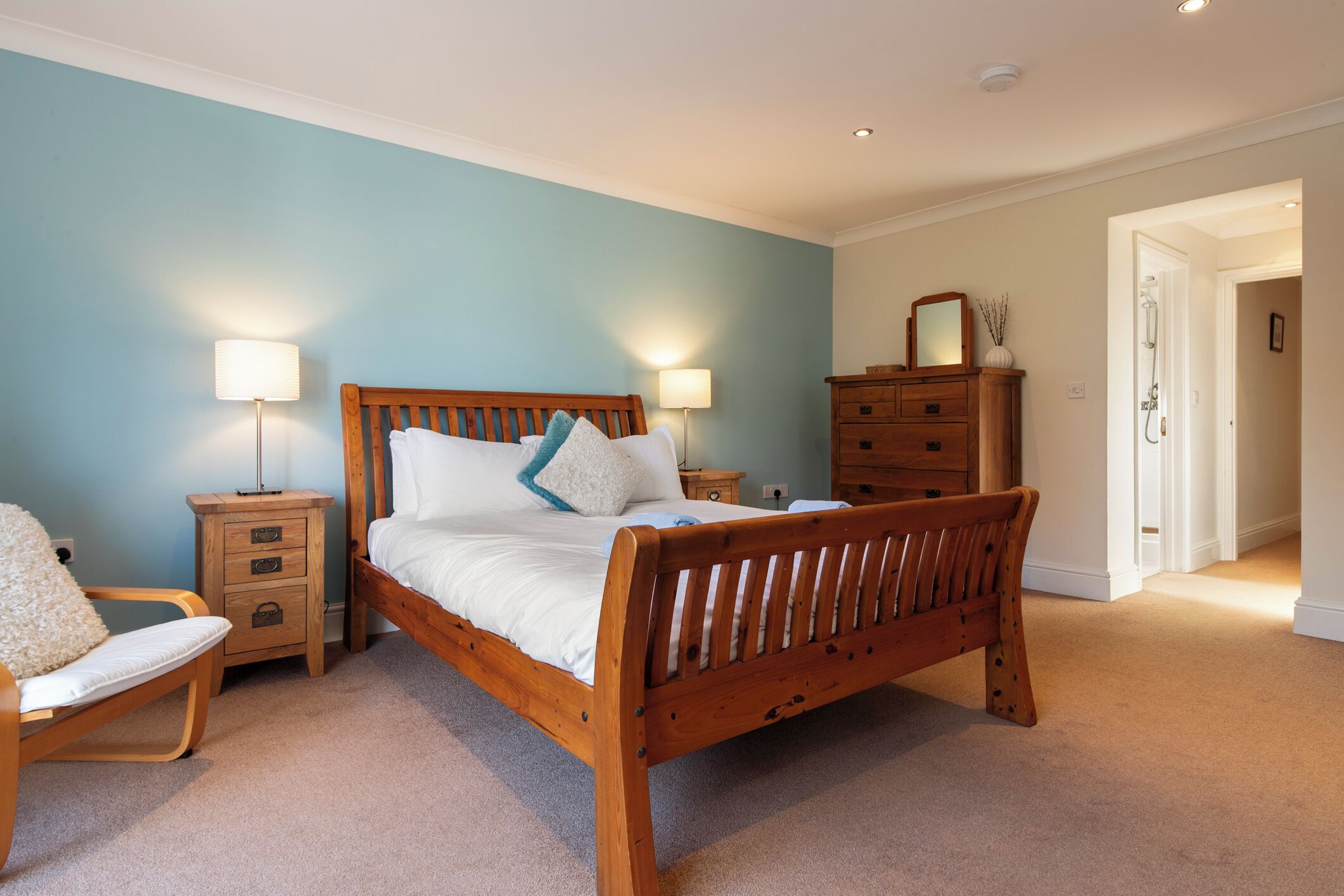 A bedroom with a wooden bed, two bedside tables with lamps, a wooden dresser, and a chair.
