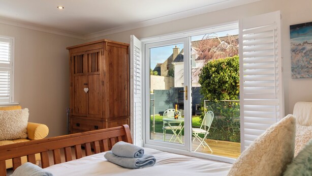 A bedroom with a bed, wooden wardrobe, and a sliding glass door leading to an outdoor patio. - Daisy Cottage - St Florence, Parking, (Saint Florence)