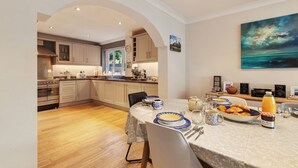 A modern kitchen with wooden flooring, a dining table set with plates, glasses, and a coffee pot. - Daisy Cottage - St Florence, Parking, (Saint Florence)