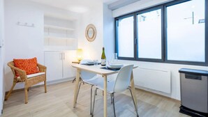 Une cuisine moderne avec une table à manger, des chaises, un fauteuil en osier, un radiateur et une grande fenêtre.