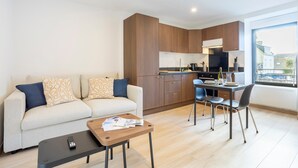 Un appartement moderne comprenant un canapé, une table à manger avec des chaises, un coin cuisine et une grande fenêtre.