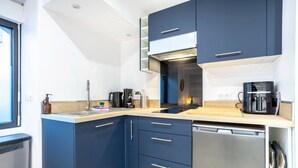 Een kleine keuken met donkerblauwe kastjes, een roestvrijstalen vaatwasser en een koffiezetapparaat.