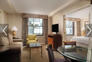 Ein Hotelzimmer mit Sofa, gelbem Sessel, Glastisch, Fernseher und Bett.