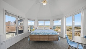 A bedroom with a bed, a table, and chairs, large windows with a view of the beach and buildings. - Moon Palace: Oceanfront | Elevator | Hot Tub | Private Pool | Game Room (Salvo)