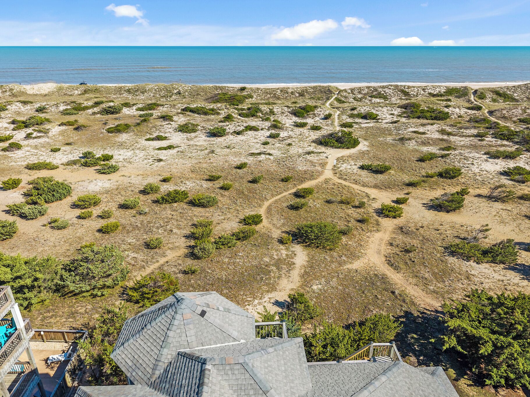 A coastal property with a sandy beach, sparse vegetation, and a clear view of the ocean.