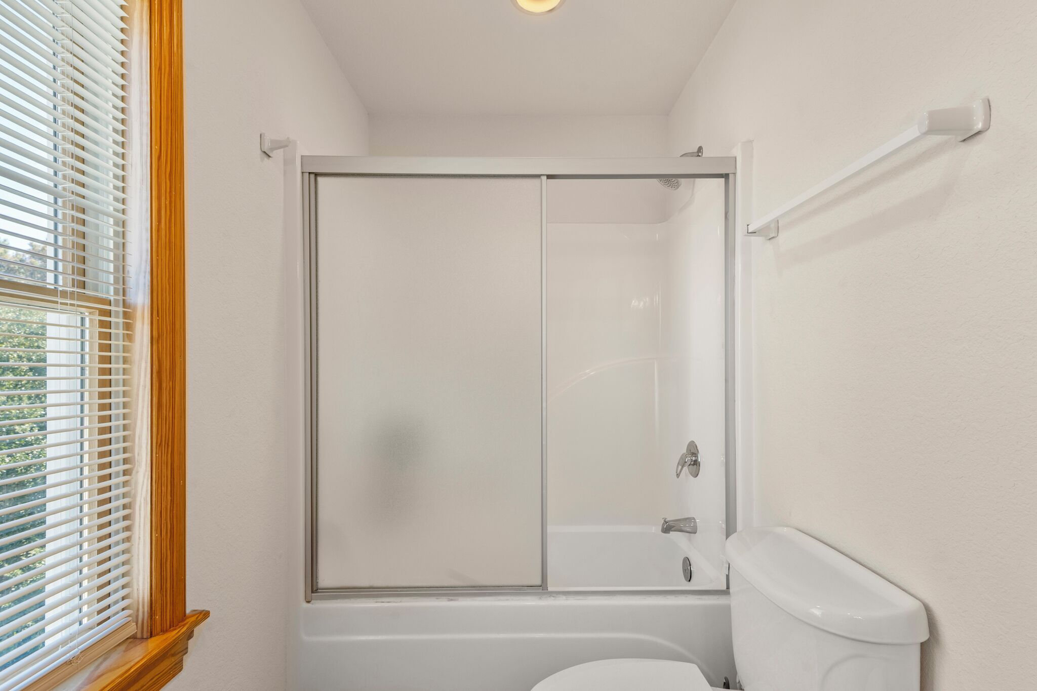 Ein Badezimmer mit Duschkabine aus Glas, einer weißen Toilette und einem Fenster mit Rollo.