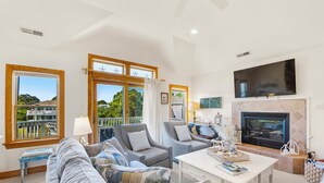 A spacious living room with a large window, a fireplace, and a flat-screen TV. - Marga-Lisa: Private Pool | Wet Bar | Ensuite Bedrooms (Corolla)