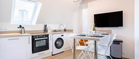 Une cuisine moderne équipée d’un lave-linge, d’un four et d’un coin repas avec des chaises et une table.