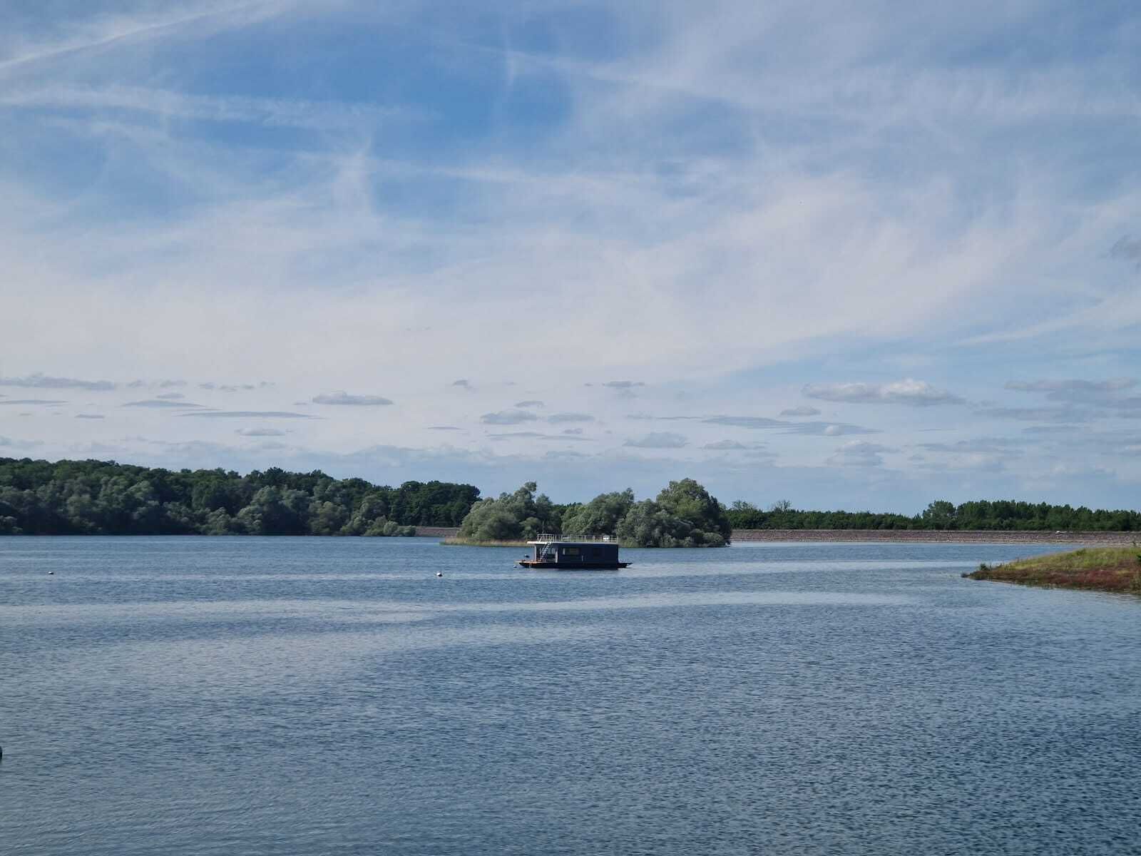 A calm lake with a small boat in the center, surrounded by dense trees and a clear sky.