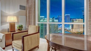A hotel room with a dining area, a lamp, a vase, and a view of a cityscape at night. - F1 View + Strip Views, 34th Floor at MGM Signature (Las Vegas)