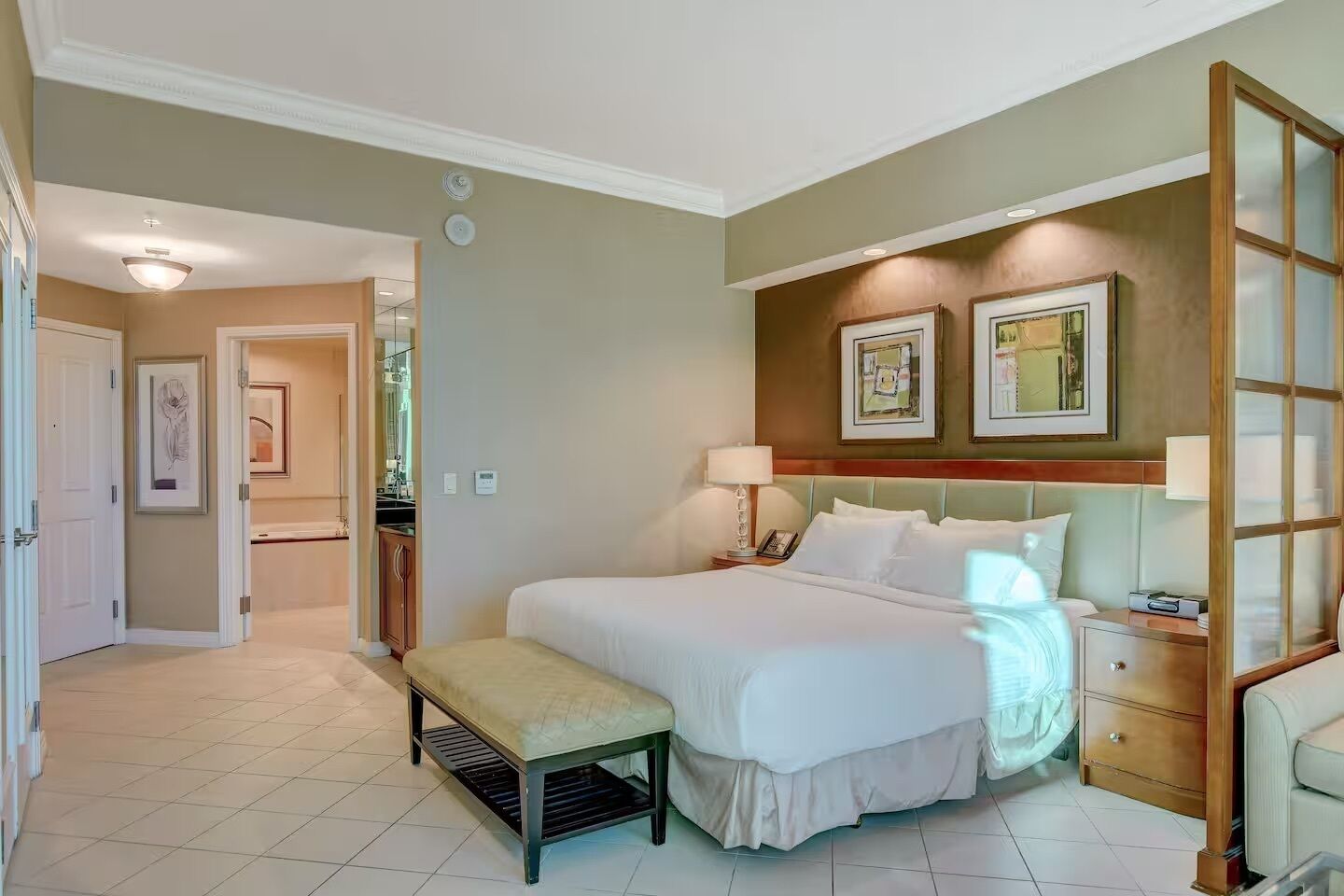 A hotel room with a large bed, bedside tables, a bench, and artwork on the walls.