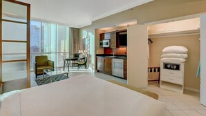 A hotel room with a large bed, a dining area with a table and chairs, a kitchenette, and a view of the city through large windows. - F1 View + Strip Views, 34th Floor at MGM Signature (Las Vegas)