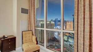 A room with a large window offering a city view, a tufted armchair, and a small wooden nightstand. - F1 View + Strip Views, 34th Floor at MGM Signature (Las Vegas)
