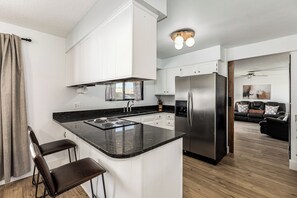 Una cocina moderna con gabinetes blancos, un refrigerador de acero inoxidable y una encimera negra.