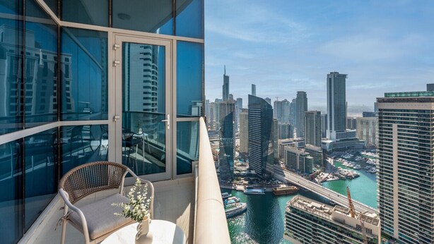 Un edificio alto con balcón que da a un puerto deportivo y al horizonte de la ciudad.