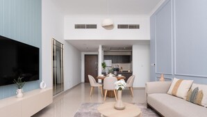 Una sala de estar moderna con televisor de pantalla plana, un comedor con mesa y sillas, y una cocina al fondo.