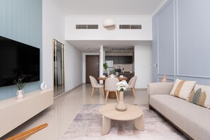 Ein modernes Wohnzimmer mit Flachbildfernseher, einer Couch, einem Esstisch mit Stühlen und einer Küche im Hintergrund.