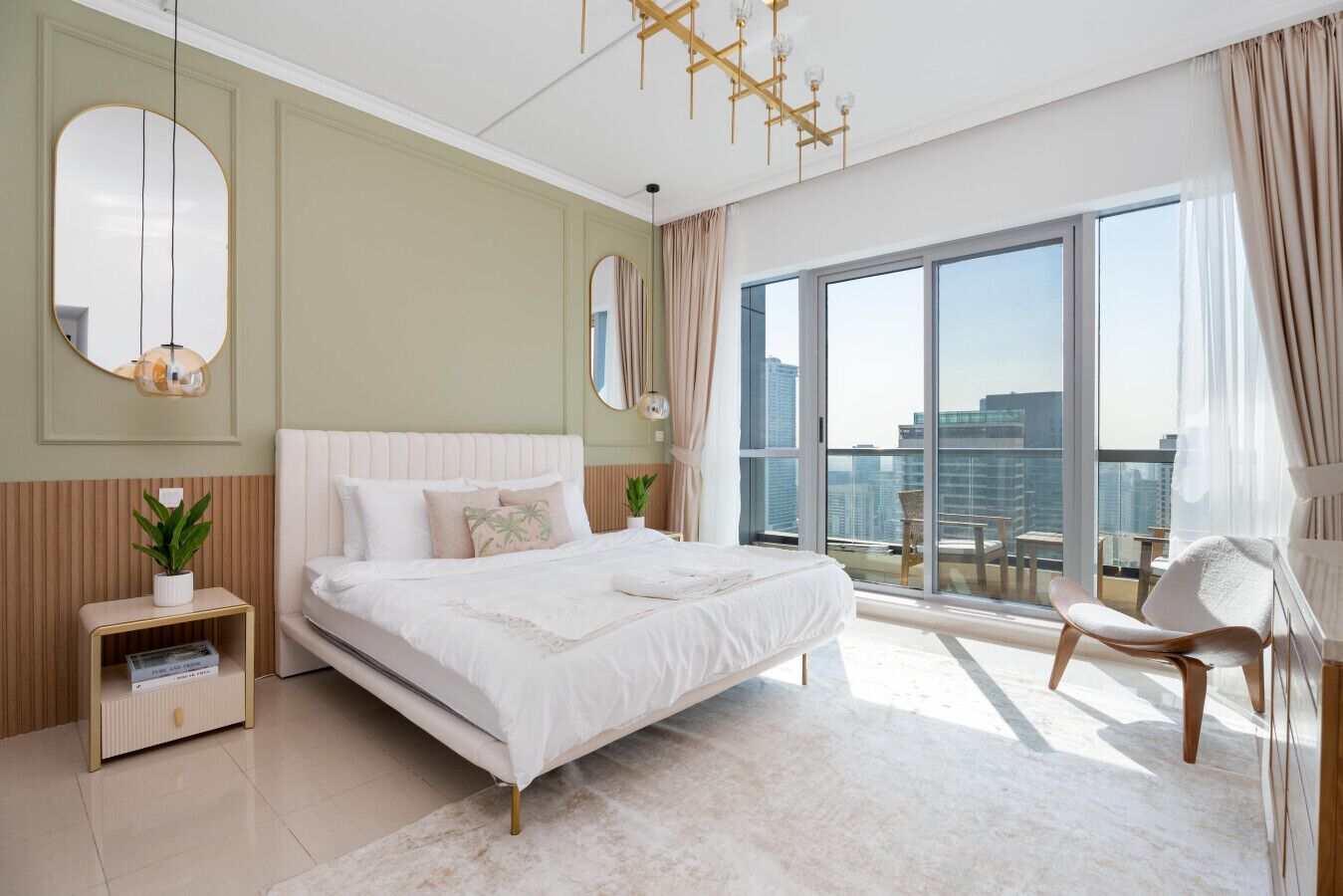 Une chambre moderne avec un grand lit, un coin salon avec un fauteuil et une vue sur la ville grâce à de grandes fenêtres.