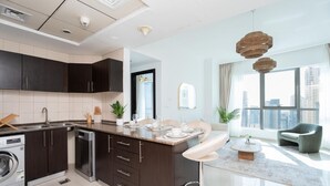Una cocina moderna con muebles oscuros, lavavajillas integrado y comedor con mesa de vidrio y sillas blancas.