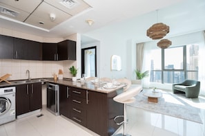 A modern kitchen with dark cabinetry, a built-in dishwasher, and a dining area with a glass table and white chairs. - Dreamy 2BR at Dubai Marina (Dubai)