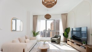 Una sala de estar moderna con sofá, sillón, mesa de centro, televisor y ventanas amplias con vista a la ciudad.
