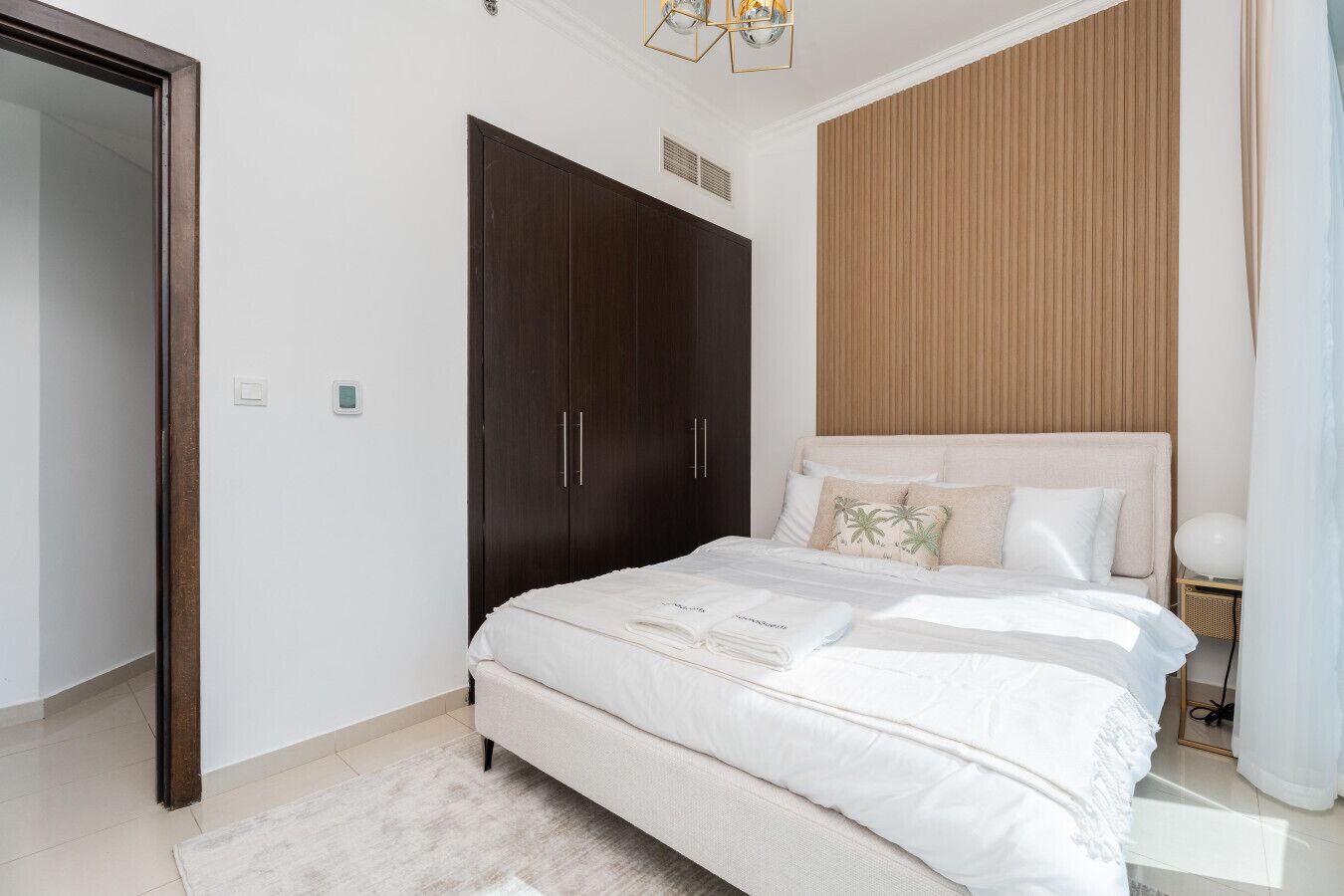 A bedroom with a large bed, dark wooden wardrobe, and a light-colored headboard.