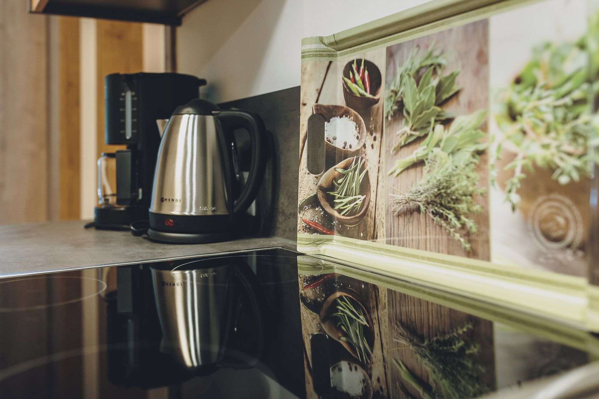 A kitchen counter with a stainless steel coffee maker and a framed picture of herbs.