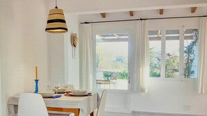 Spiseområde med et bord dækket til fire personer, en hængende lampe og udsigt til grønne omgivelser.