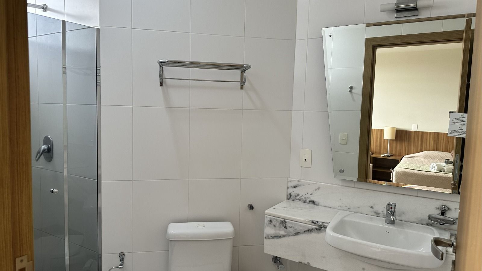 A bathroom with a glass shower enclosure, a toilet, a sink with a marble countertop, and a mirror above the sink.