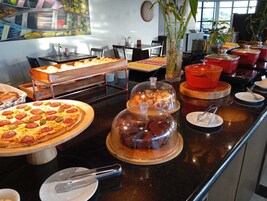 A buffet with various food items, including a pizza, covered desserts, and a variety of other dishes.