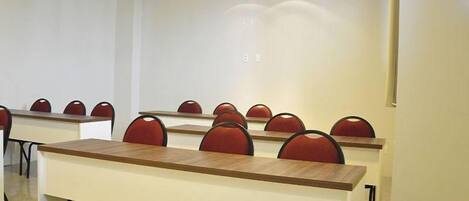 Un salón de conferencias con varias mesas y sillas, paredes blancas e iluminación en el techo.