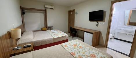 A hotel room with two beds, a desk, a TV, and a bathroom visible through an open door.