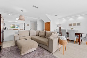 A modern living room with a sectional sofa, a dining area with a table and chairs, and a kitchen in the background.
