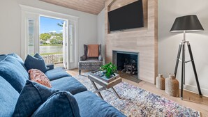 Ein Wohnzimmer mit einer Couch, einem Couchtisch mit Pflanze, einem Kamin und einem an der Wand montierten Fernseher.