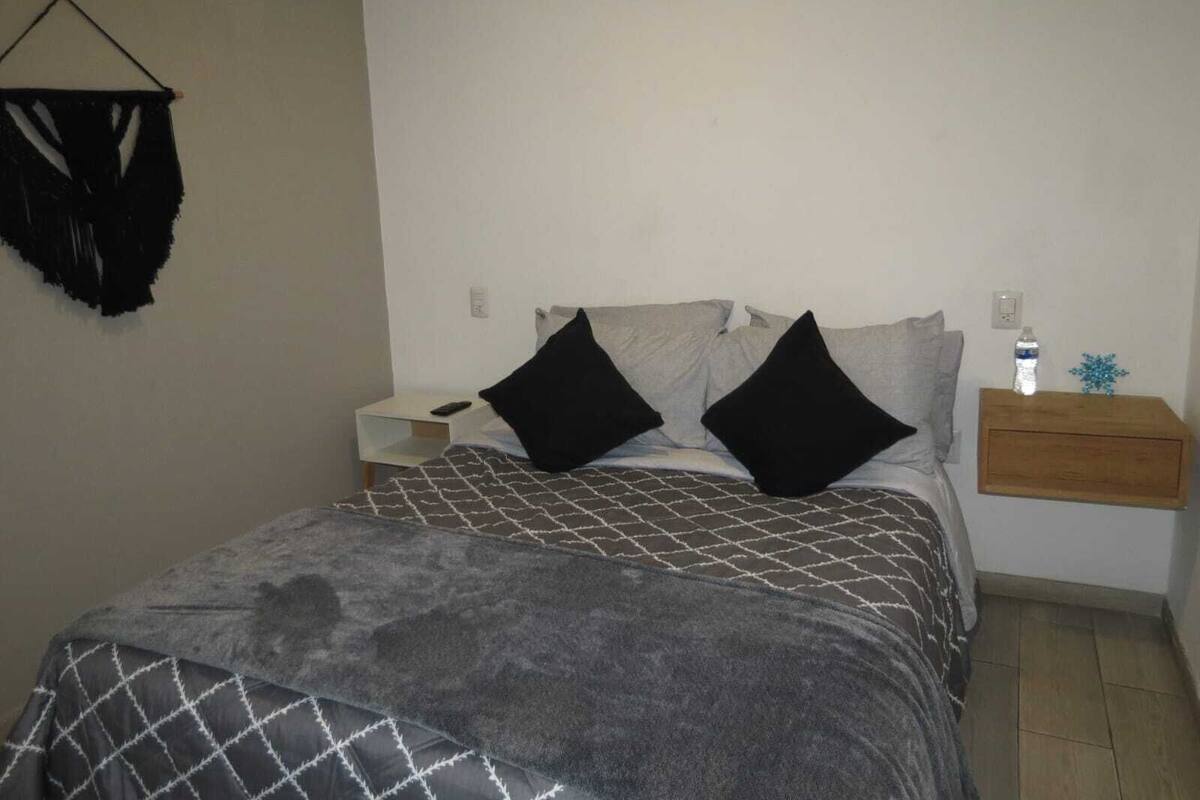 Ein Schlafzimmer mit einem Bett, zwei Nachttischen, einer Wandleuchte und einem kleinen Holztisch mit einer Wasserflasche und einem dekorativen Gegenstand.