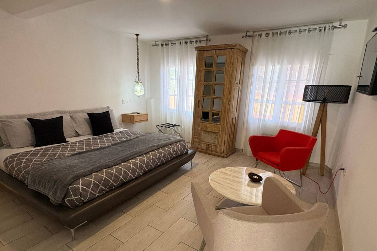Ein Schlafzimmer mit einem Bett, einem Holzschrank, einem roten Sessel und einem kleinen Tisch.