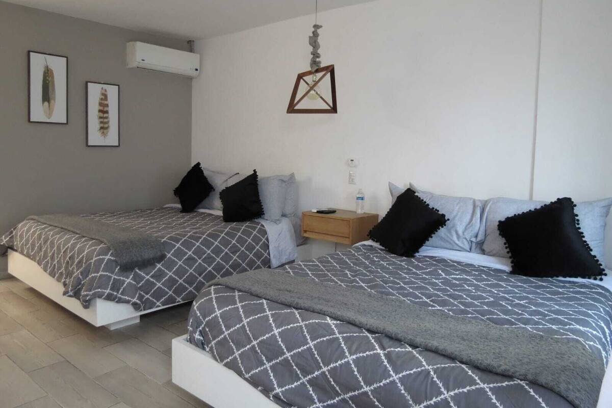 Ein modernes Schlafzimmer mit zwei Betten, einem Holznachtkästchen und einer hängenden Leuchte.