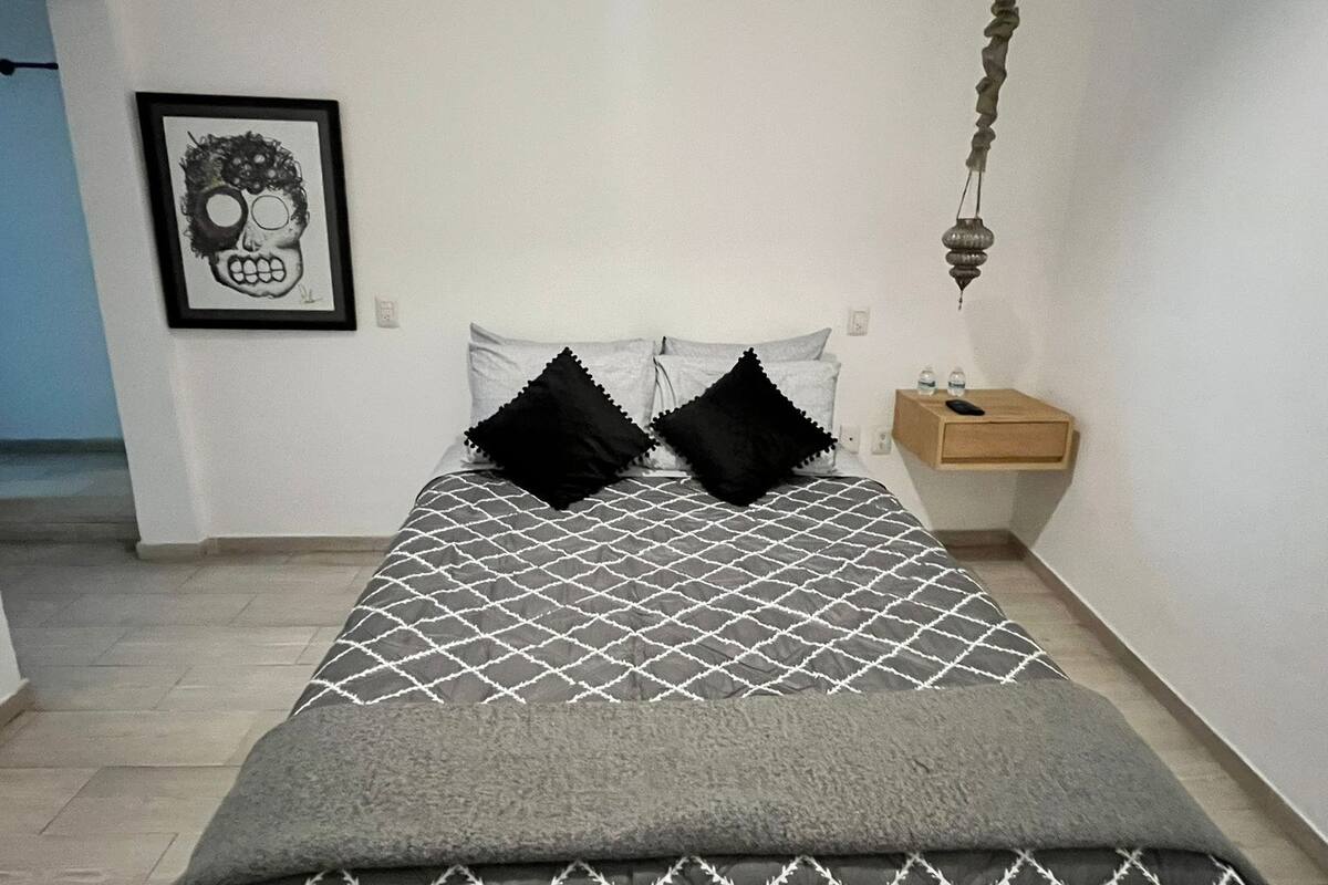 Ein Schlafzimmer mit Bett, Kissen, Nachttisch, gerahmtem Bild und einer Pendelleuchte.