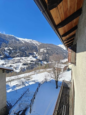 Un paisaje montañoso nevado con un pueblo en la falda, visto desde un balcón con barandilla de madera.
