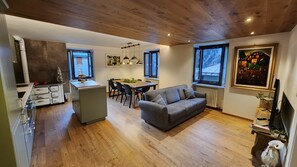 Een moderne keuken met een centraal eiland, een eethoek met een tafel en stoelen, een grijze bank en grote ramen met uitzicht.