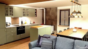 Een compacte keuken met een centraal eiland, een eettafel met stoelen, en een bank met kussens.